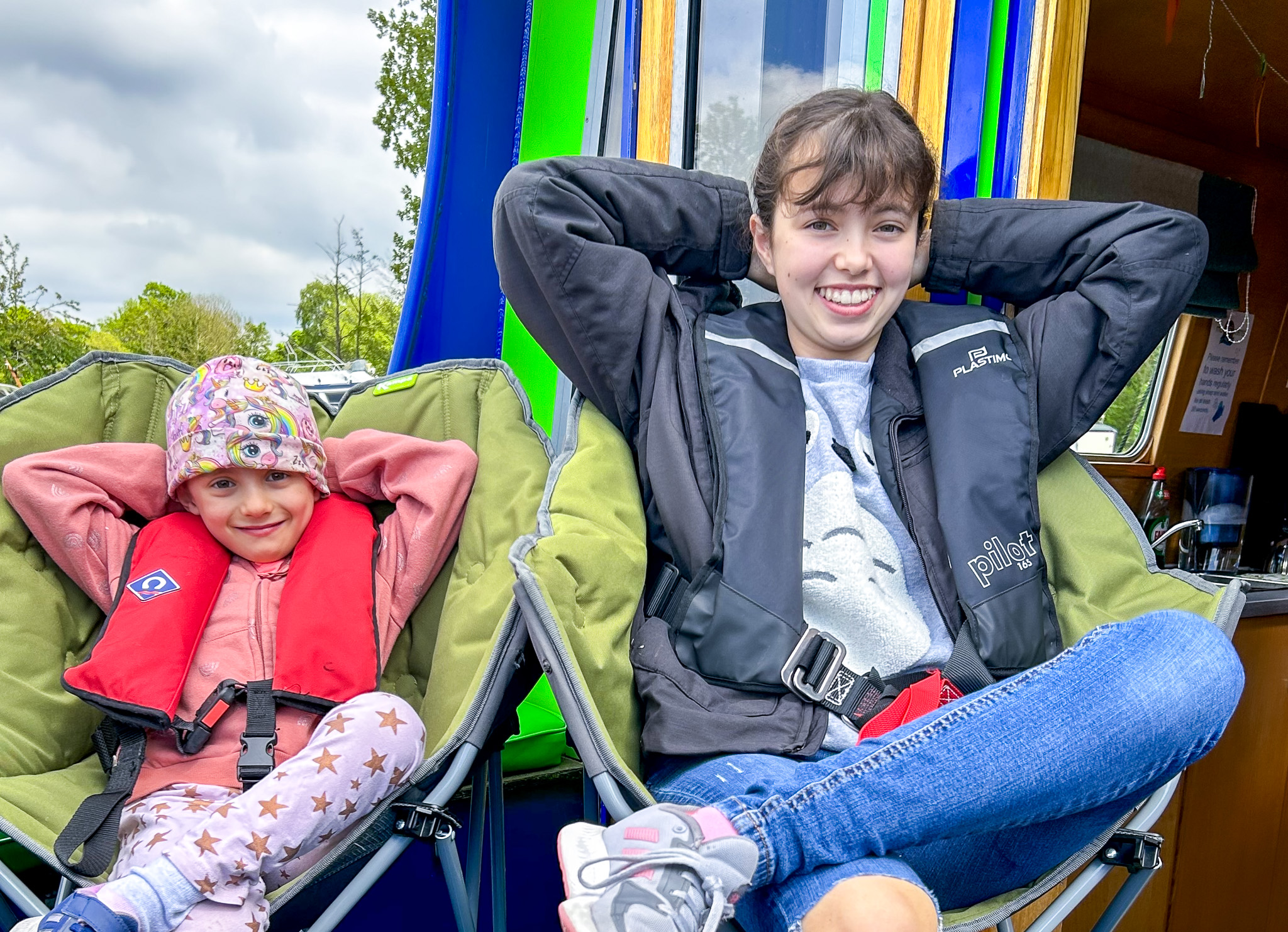 Two sisters sit with arms behind their heads on camping chairs on the Momentum boat.